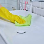 Close-up of cleaning sink with faucet in bathroom, female hands in rubber protective gloves with cleaning detergent and professional rag. Housekeeping housework housecleaning cleaning service concept